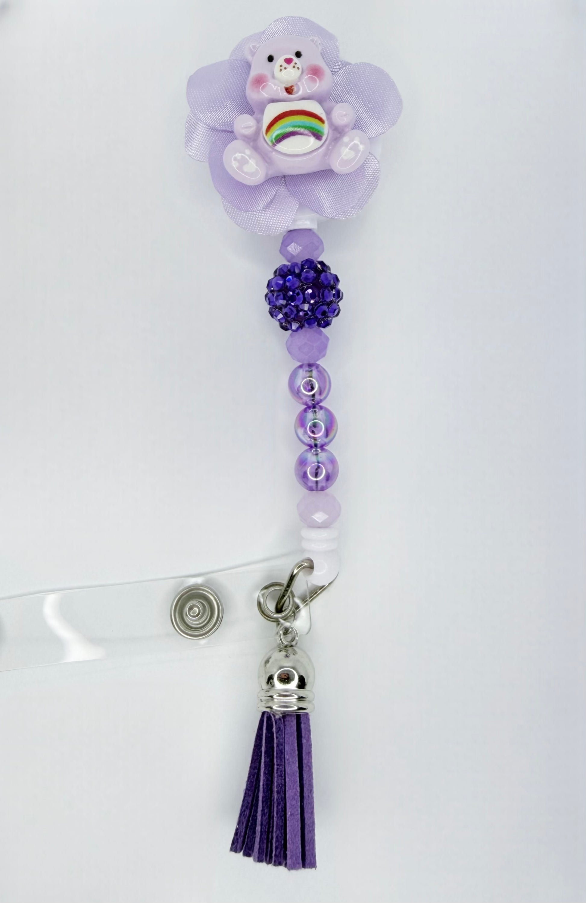 Purple decorative clip with a teddy bear charm, beads, and tassel on a white background