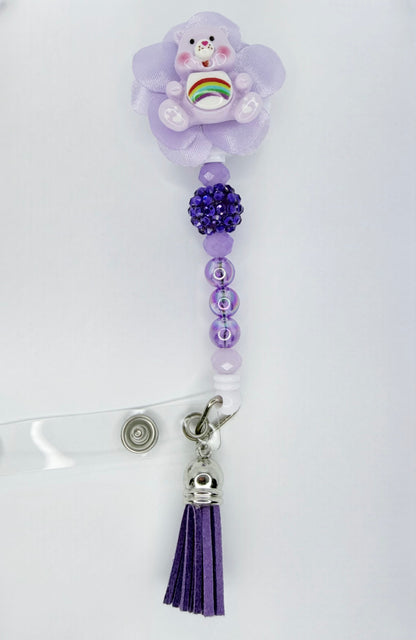 Purple decorative clip with a teddy bear charm, beads, and tassel on a white background